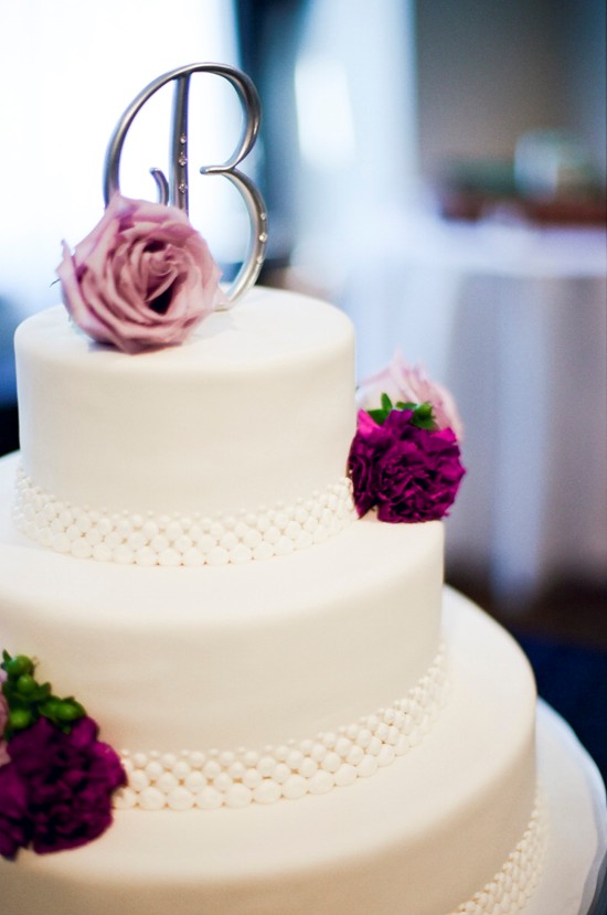 Three tiered wedding cake with pearl trim and purple flowers