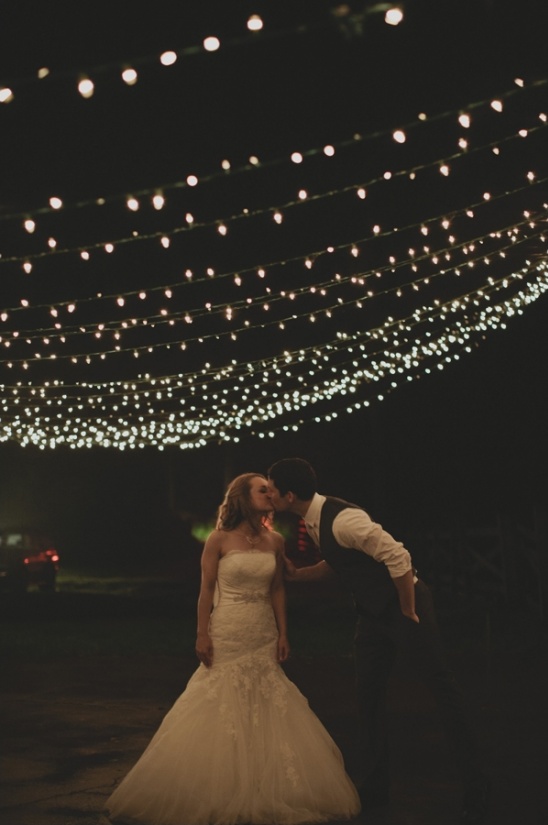 Bride and groom kissing under string lights at night wedding