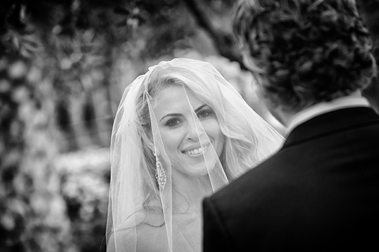 Bride veiled, smiling at groom during wedding ceremony