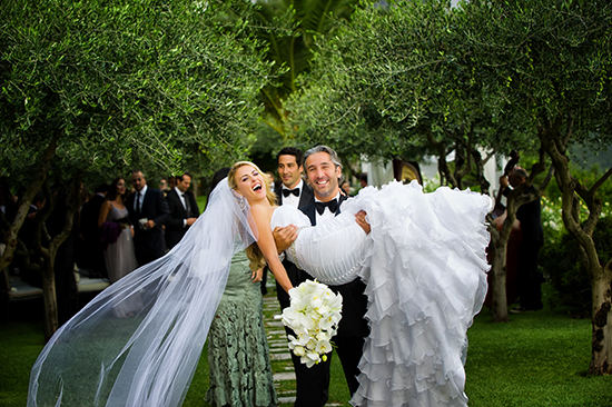 Happy bride carried by groom amidst olive trees