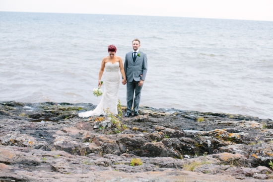 Bride and groom holding hands on rocky shore, ocean background