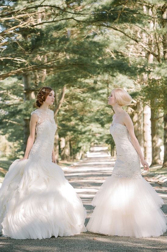 Two brides in elegant wedding gowns outdoors in sunlight