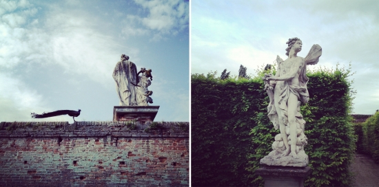 Two classical statues and a peacock on a brick wall beneath the sky
