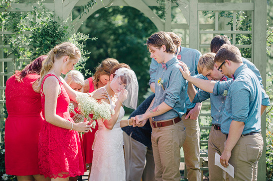 Bride and groom praying with wedding party during outdoor ceremony