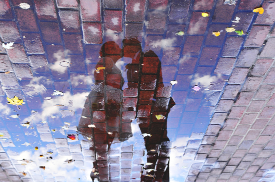 Romantic couple reflected in a puddle on brick pavement