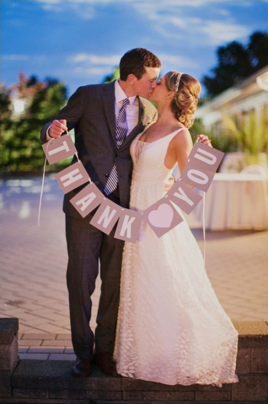 Newlyweds kissing holding Thank You banner at wedding