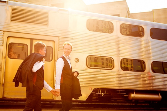 Grooms holding hands in front of commuter train