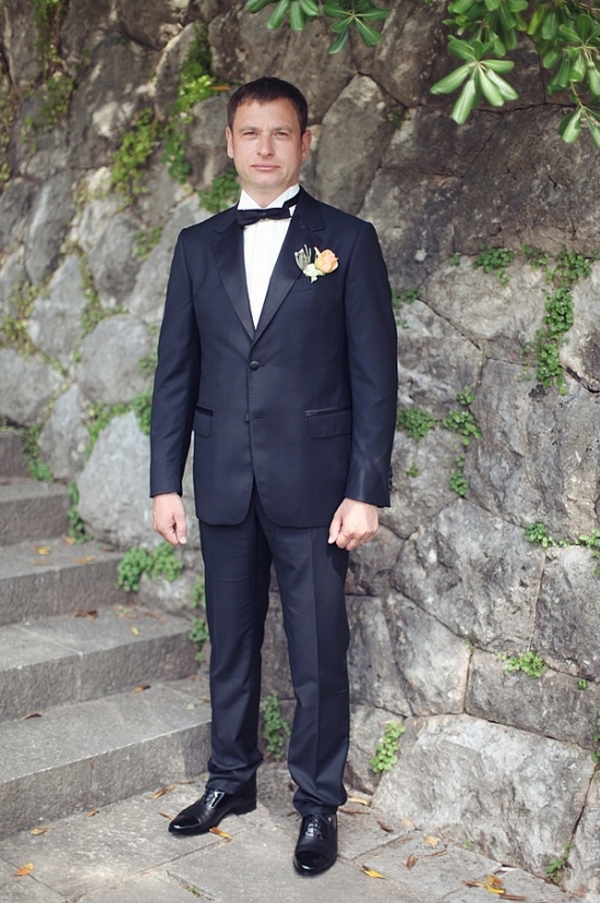Handsome groom in elegant suit stands by stone wall