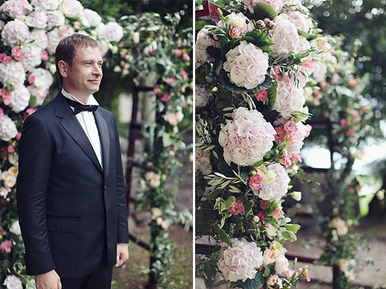 Groom in tuxedo at wedding with floral arch background