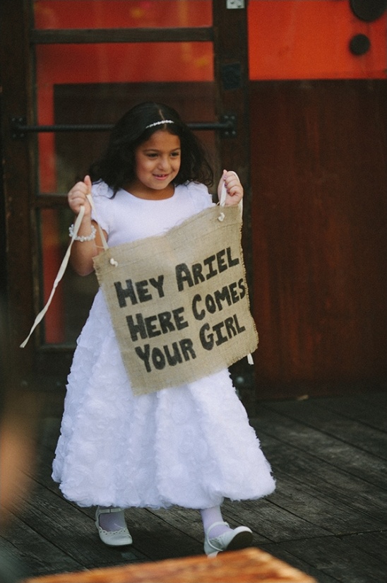 Flower girl holds sign Hey Ariel Here Comes Your Girl