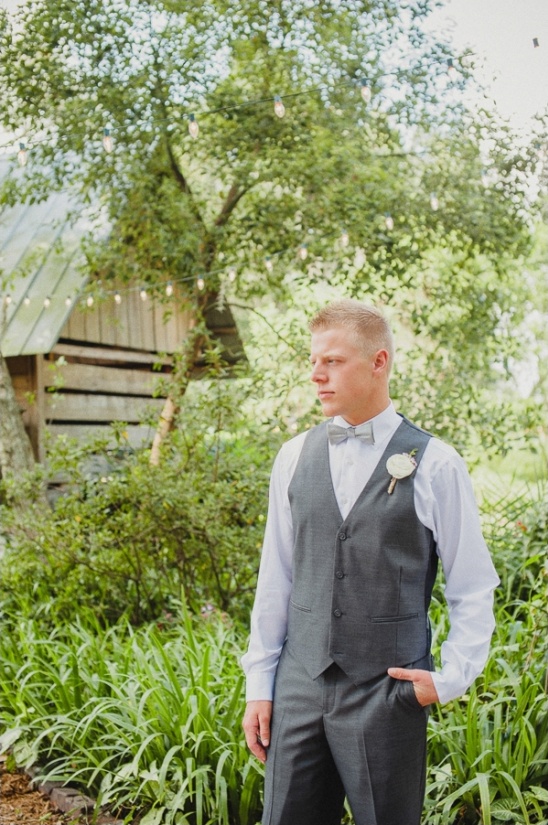 Groom in gray vest stands in outdoor wedding venue