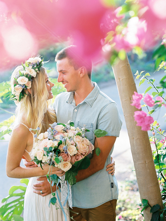 Smiling couple embraces in a garden setting with flowers and bouquet