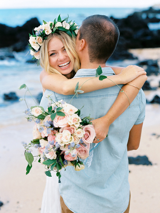 Bride and groom share a hug with bouquet at beach wedding