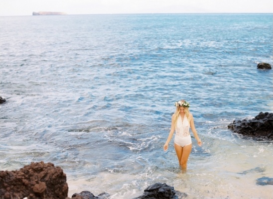 Blonde woman in white dress walking in ocean water with flower crown