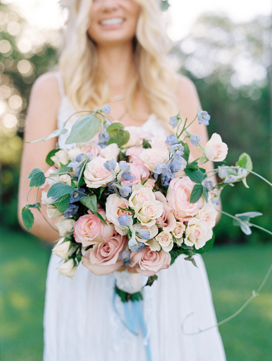 Bride holding a pastel rose bouquet on a blurred green background