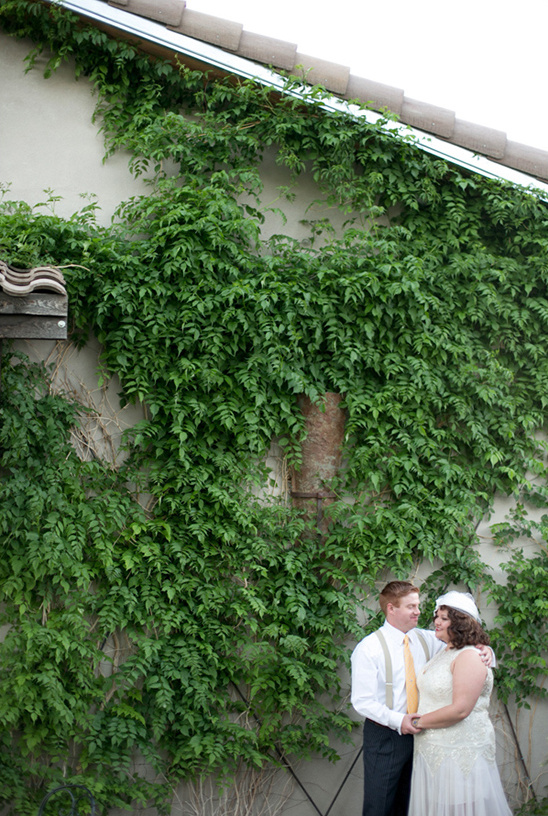 Wedding couple poses in front of a green vine covered wall
