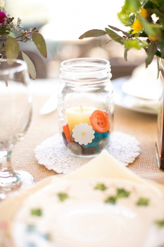 Mason jar centerpiece with candle and colorful buttons on a table
