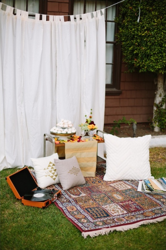 Cozy outdoor picnic setup with rug, pillows, record player and decorations