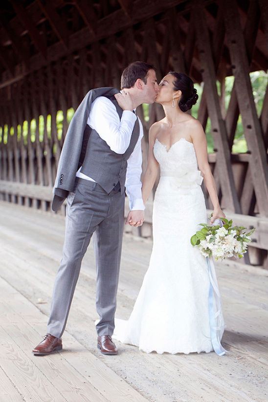 A newly married couple shares a kiss on a wooden bridge at their wedding