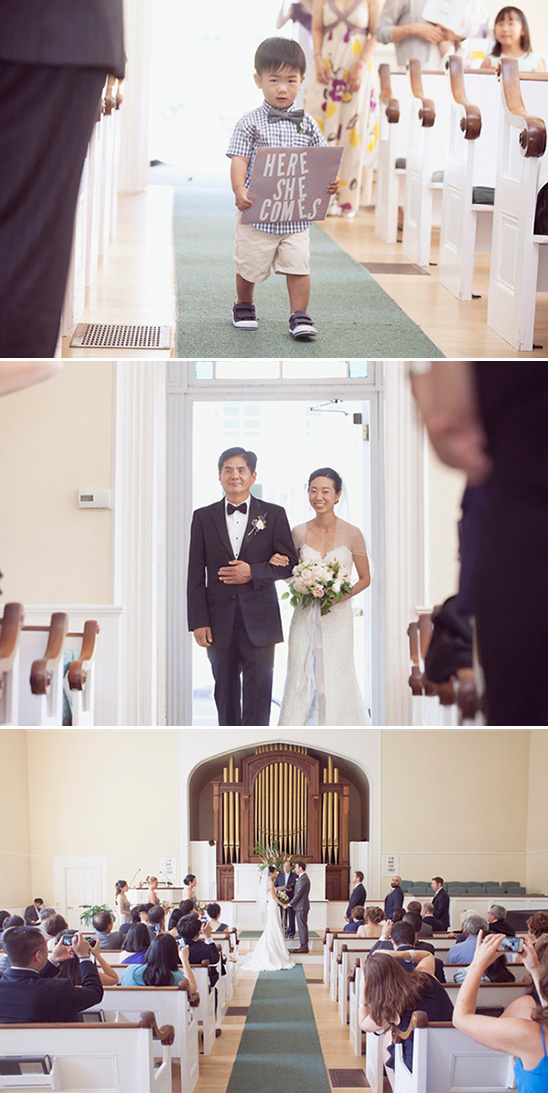 Wedding ceremony with a flower girl holding a Here She Comes sign