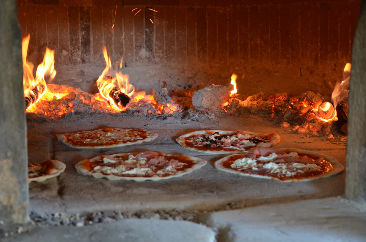 Pizzas baking in a wood-fired oven, flames in the background