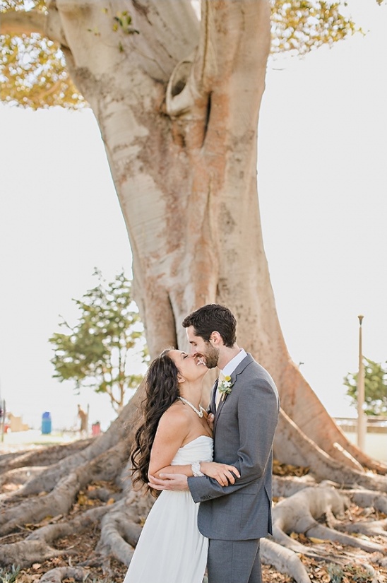 Bride and groom share a kiss under a big tree after the wedding