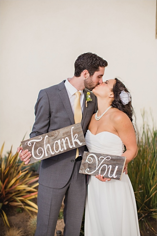 Newlywed couple kissing while holding thank you signs at wedding