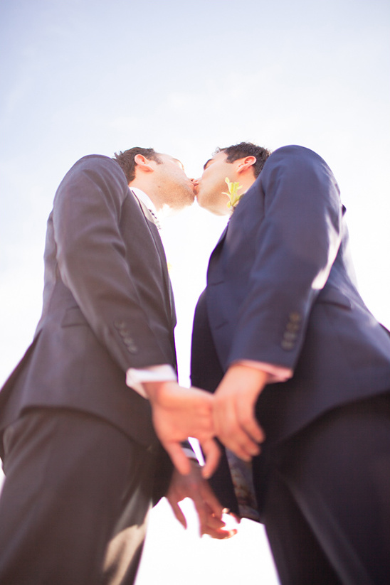 Two grooms sharing a kiss on their wedding day with holding hands