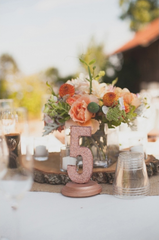 A rose gold table number five with a flower arrangement