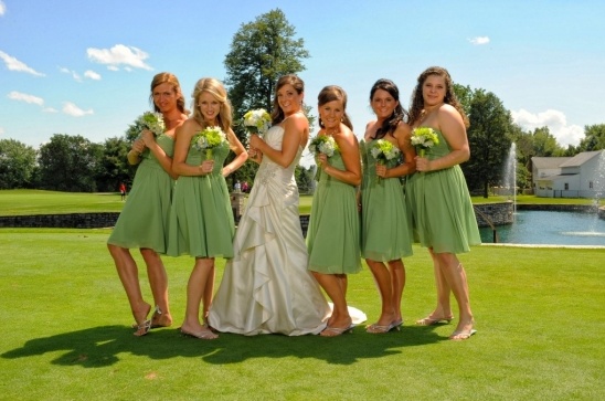 Bride and bridesmaids posing on golf course with green dresses
