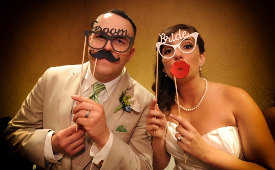 Happy bride and groom posing with photo booth props at their wedding