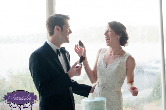 Happy bride and groom laugh while playfully eating wedding cake