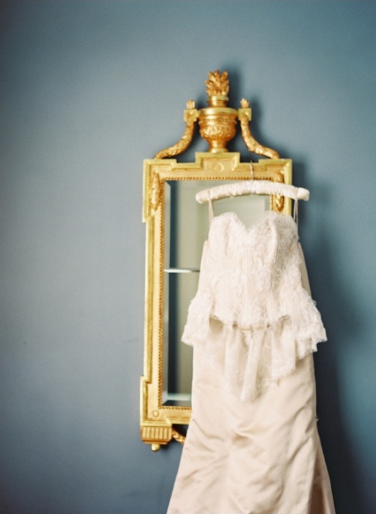 Elegant lace wedding dress hanging on ornate mirror