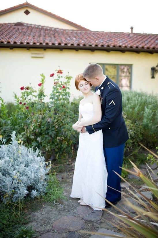 Groom in uniform embraces bride at outdoor wedding