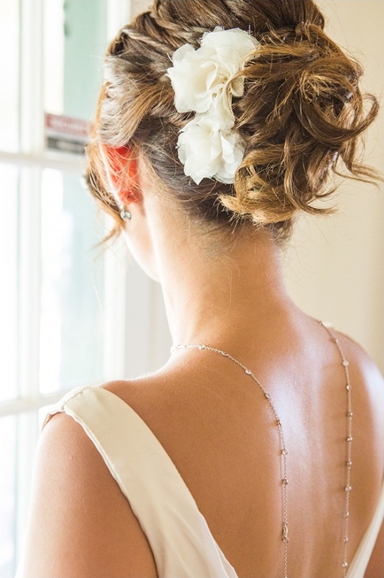 Elegant bridal updo with flower detail and delicate back necklace