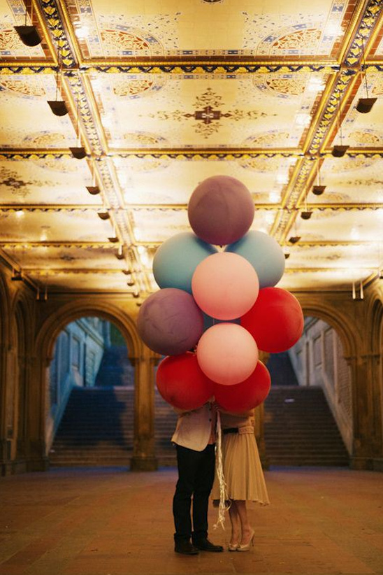 Couple hides behind colorful balloons under ornate ceiling