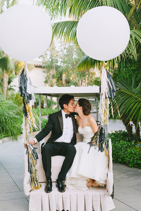 Bride and groom kissing in golf cart with balloons