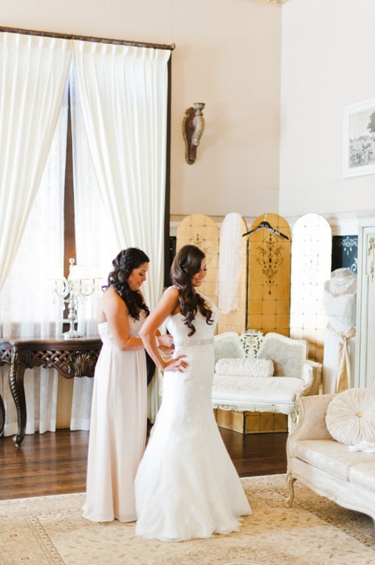 Bride getting ready helped by bridesmaid in bridal suite