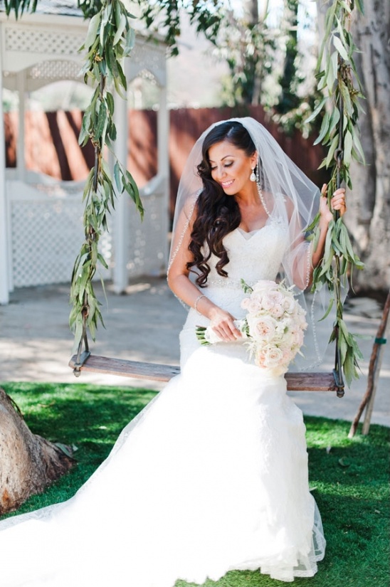 Brunette bride in white gown on swing holding bouquet