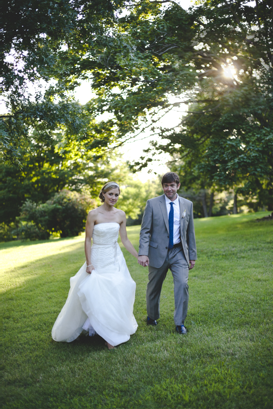 Bride and groom stroll through sun dappled lawn