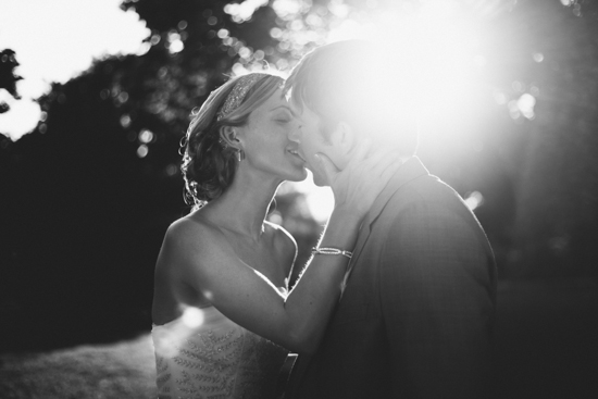 Bride and groom share a kiss backlit by sunlight
