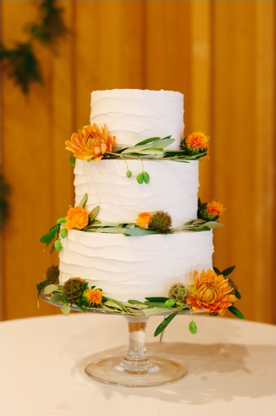 Three-tiered wedding cake adorned with orange flowers and greenery