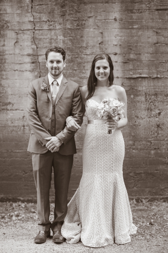 Newlyweds pose against a rustic wall on their wedding day
