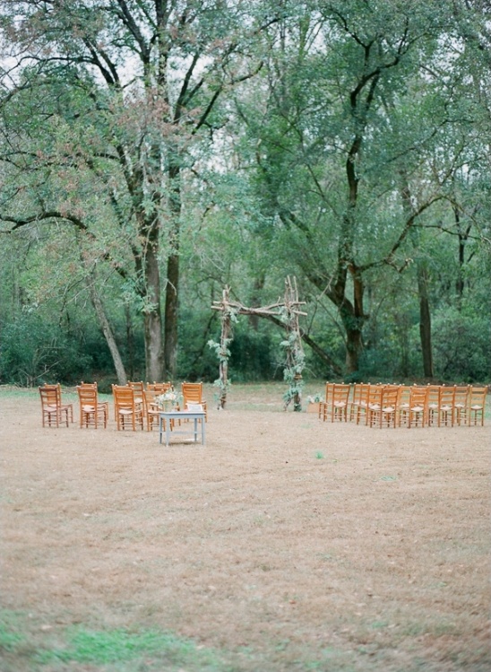 Outdoor wedding setup in a forest clearing with wooden chairs