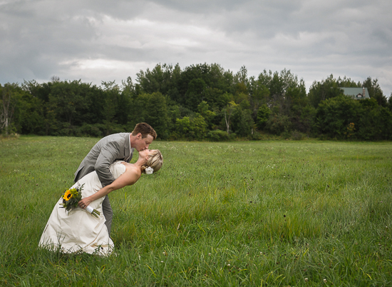 Romantic wedding kiss in a green field with a dramatic sky