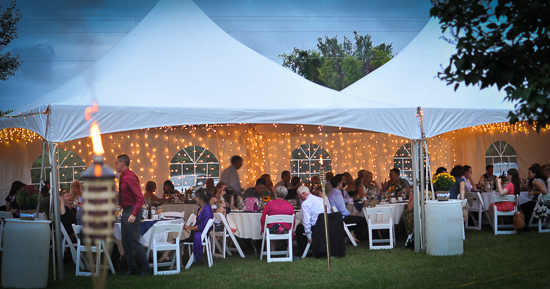 Guests enjoying a party under a tent decorated with lights outdoors