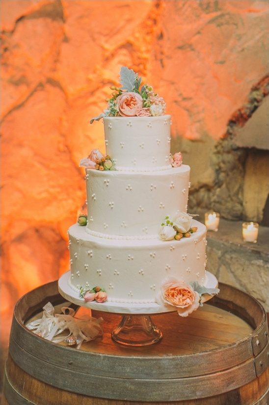 Elegant white wedding cake adorned with flowers, on a barrel