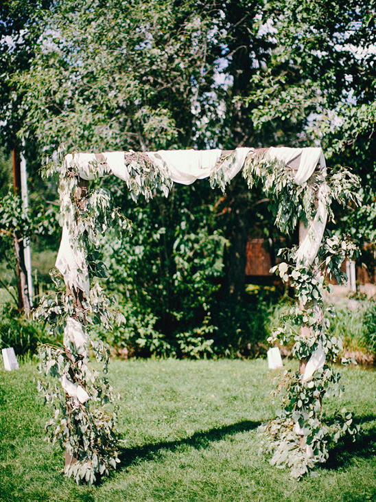 Rustic wedding arch decorated with greenery and white fabric