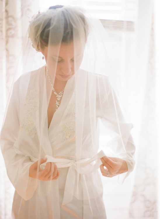Bride in white robe ties her wedding veil