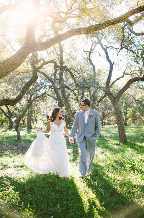 Bride and groom hold hands walking through the sunny forest on wedding day